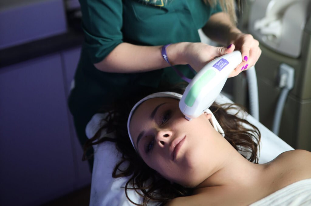 Kosmetolog wykonuje zabieg Laserem Alma Harmony DYE VL na twarzy młodej kobiety w salonie kosmetologicznym.