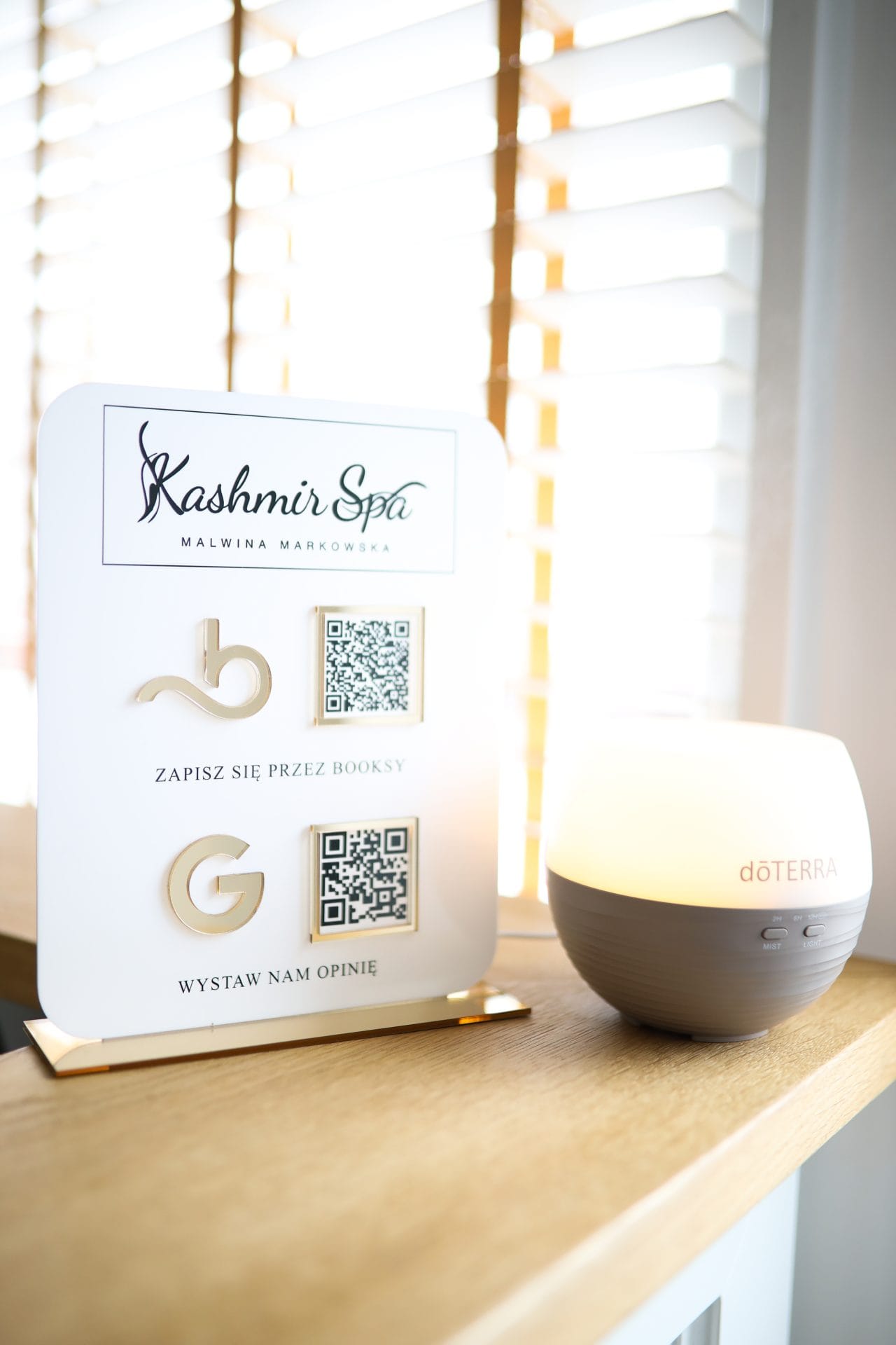 Informacyjna tablica Salonu Kashmir SPA z QR kodami do opinii usług salonu Kashmir Spa w Booksy i Google, obok eleganckiego dyfuzora.