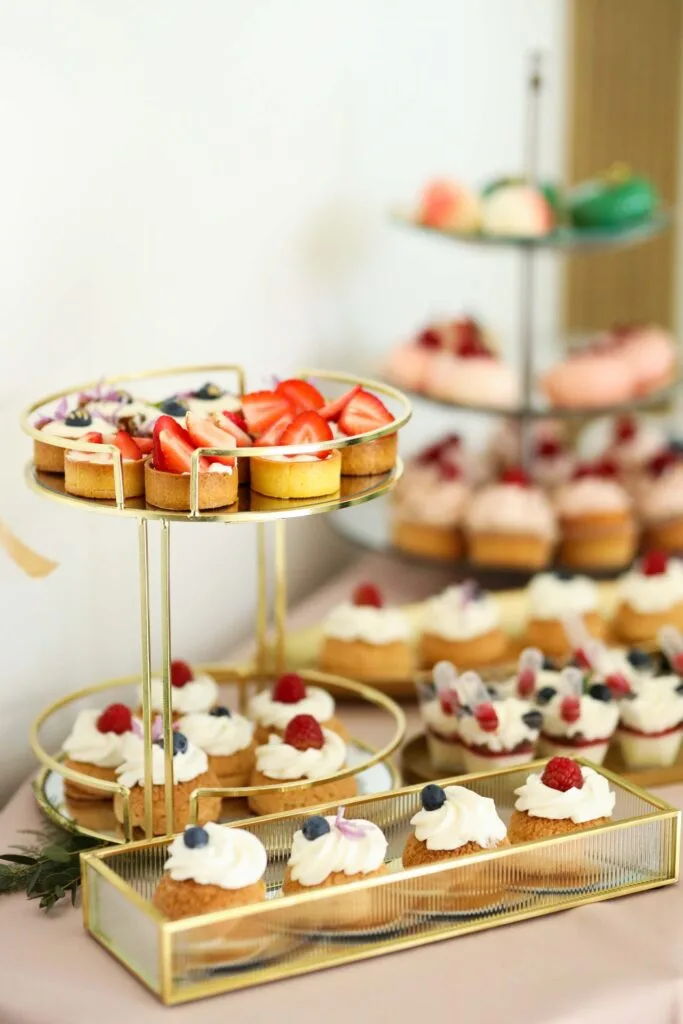 Wykwintne przekąski na złotych paterach, w tym tarty z truskawkami i ciasteczka z kremem i owocami przygotowane na 12 urodziny Kashmir SPA.