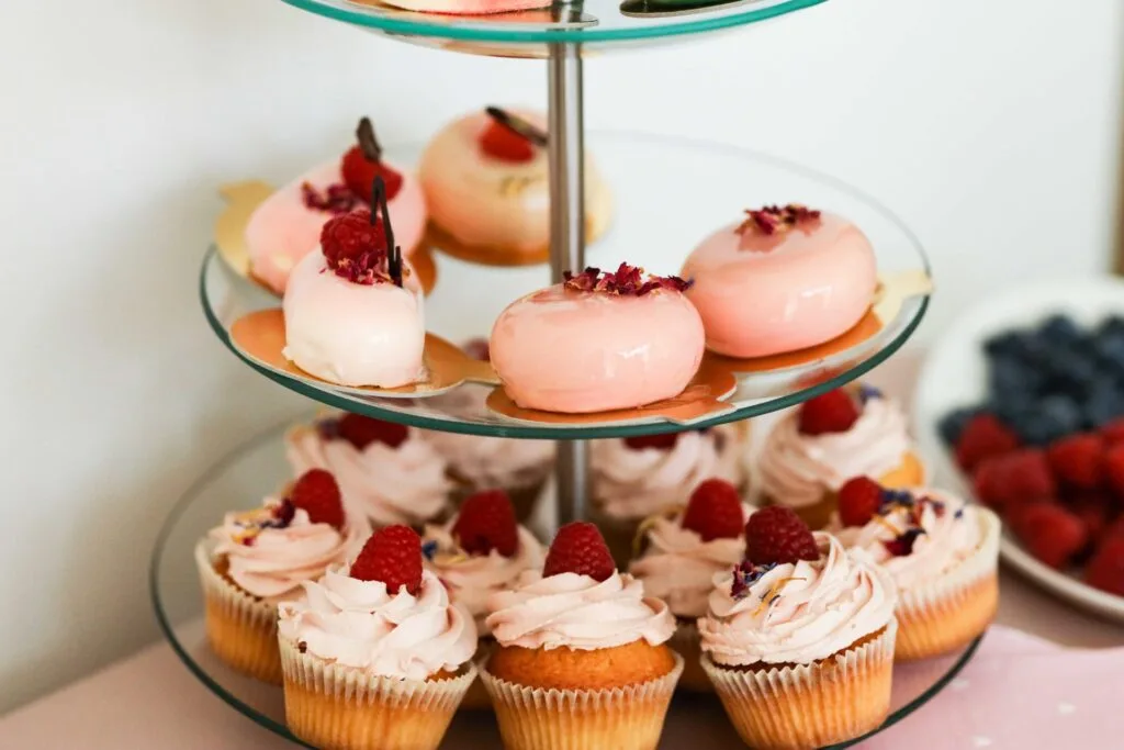 Wykwintne przekąski na złotych paterach, w tym tarty z truskawkami i ciasteczka z kremem i owocami.