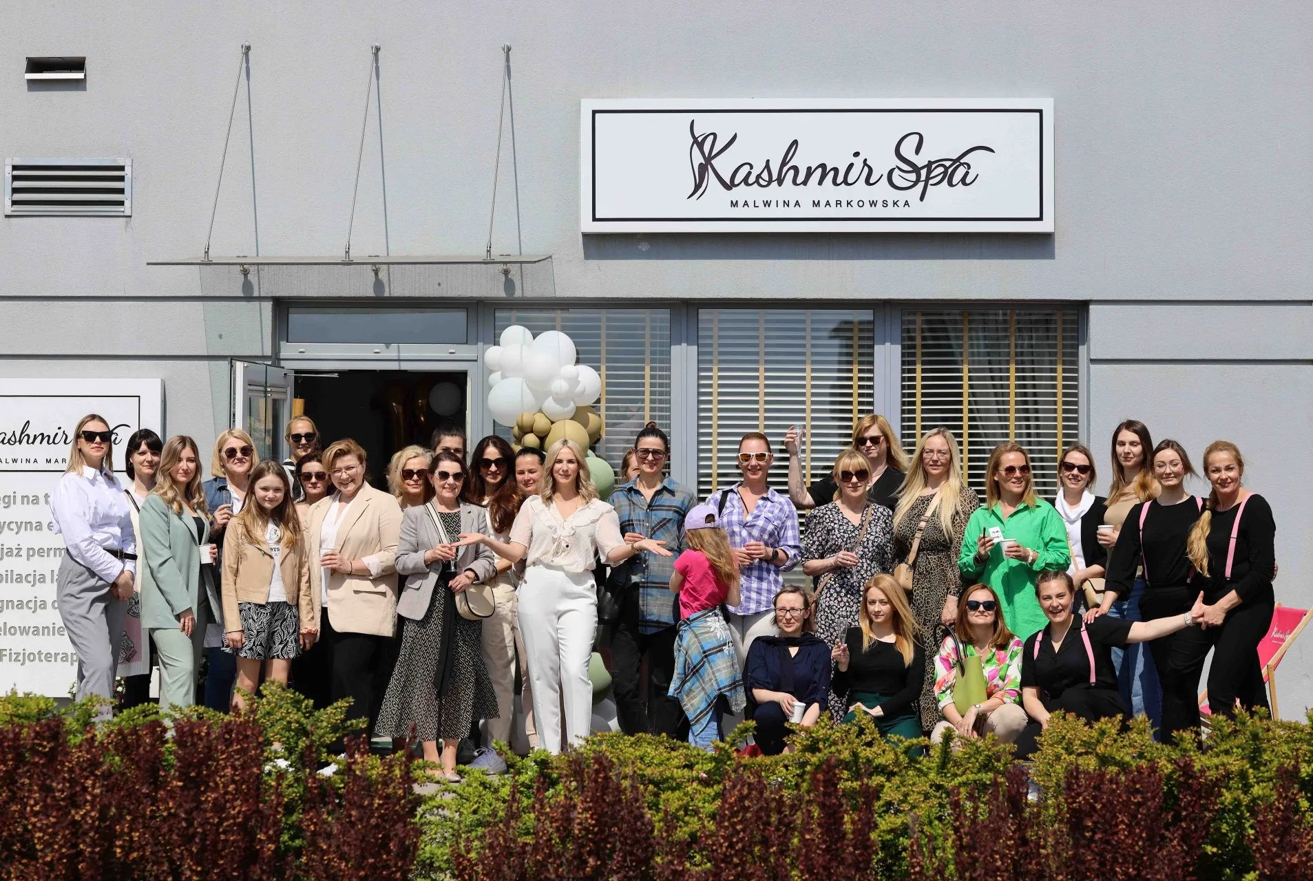 Grupa klientek celebruje 12 urodziny Kashmir SPA przed eleganckim budynkiem z balonami.