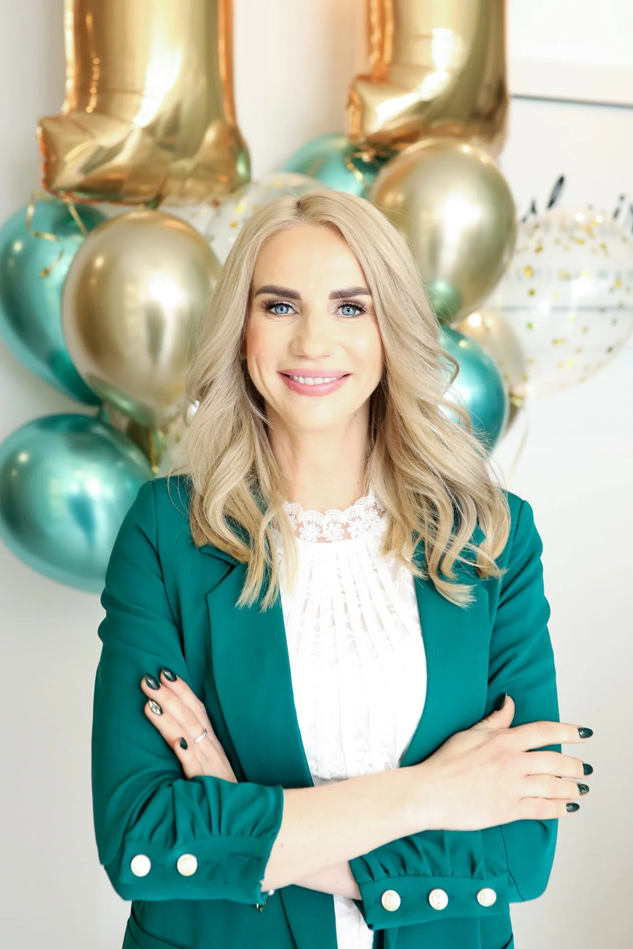 Kobieta o blond włosach w zielonej marynarce, stojąca przed balonami i złotymi cyframi "11", symbolizującymi rocznicę Kashmir SPA.