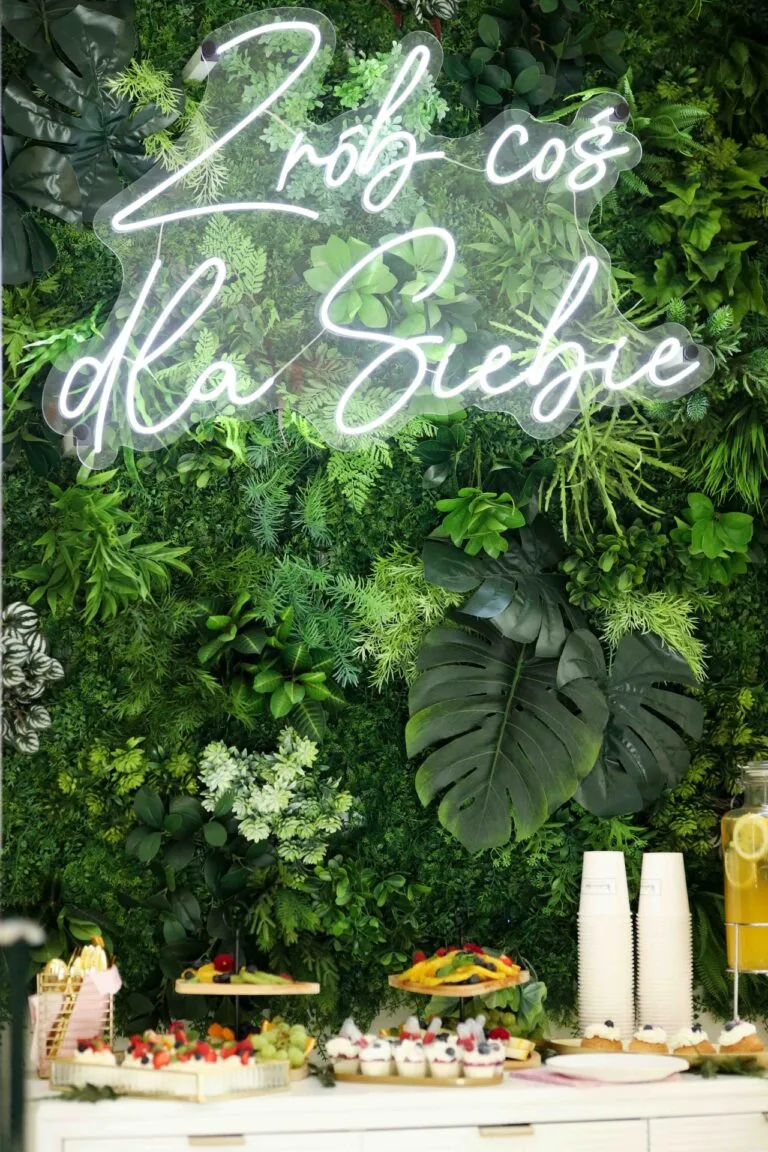 Zdjęcie ściany z bujną zieloną roślinnością i neonskim napisem "Zrób coś dla Siebie", obok przekąski i napoje podczas 12 urodzin.