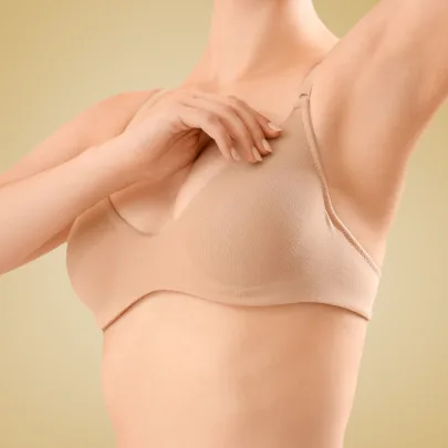 Lifting piersi - zdjęcie przedstawia kobietę w beżowym staniku dotykającą piersi